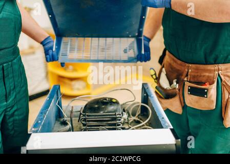 Workers in uniform removes cover of refrigerator at home. Repairing of fridge occupation, professional service Stock Photo