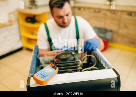Worker in uniform testing problem with refrigerator at home. Repairing of fridge occupation, professional service Stock Photo