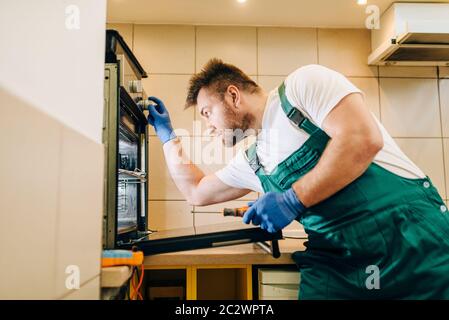 Repairman in uniform checks the oven, technician. Professional worker makes repairs around the house, home repairing service Stock Photo
