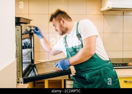 Repairman in uniform checks the oven, technician. Professional worker makes repairs around the house, home repairing service Stock Photo