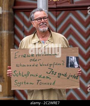 18 June 2020, North Rhine-Westphalia, Rheda-Wiedenbrück: During a vigil on the situation at the Tönnies meat factory on the market square in Rheda-Wiedenbrück, a man holds up a sign saying 'Hit the brakes again or already hit the wall? Stop the Tönnies system!'. The virus has been detected in more than 600 employees of the Tönnies meat company. The operation at Tönnies is shut down as far as possible. Photo: David Inderlied/dpa Stock Photo