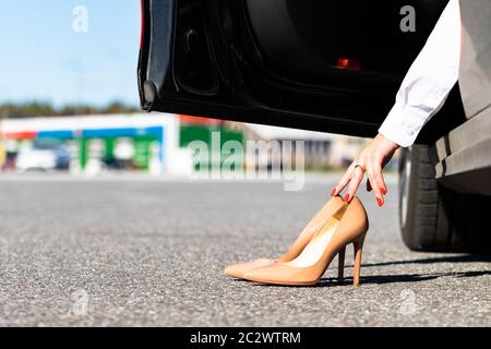 Woman changes clothes in comfortable shoes before driving, sitting in car, takes uncomfortable shoes with her hands. Stock Photo