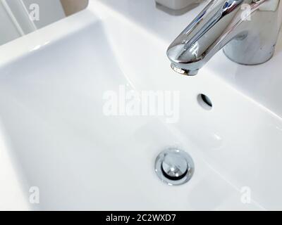 Chromed faucet with lever to mix hot and cold water on a modern white sink in a bathroom Stock Photo