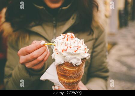 trdelnik or Trdlo with cream in the hands of a beautiful winter girl in the Czech Republic, Prague at the Christmas market Stock Photo