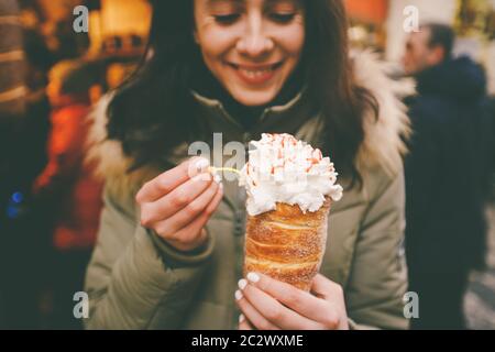 trdelnik or Trdlo with cream in the hands of a beautiful winter girl in the Czech Republic, Prague at the Christmas market Stock Photo