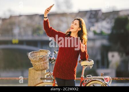 A beautiful young woman with a retro red bicycle is making a photo of herself in the old city of Europe on the River Rhine emban Stock Photo