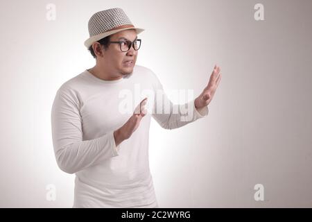 Portrait of young funny Asian man avoiding as if he is worried afraid of something bad from the side Stock Photo