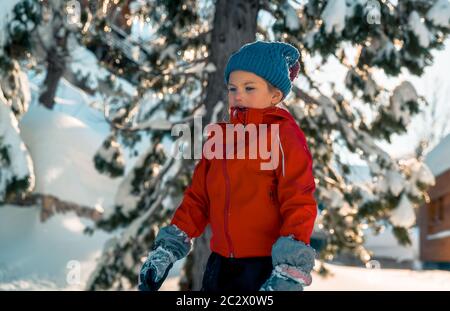 Little girl enjoying winter holidays, pretty child dressed in warm clothes having fun outdoors on backyard and playing with snow, happy winter holiday Stock Photo