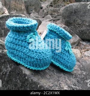 In focus arrangement of a pair of baby booties in turquoise, crocheted with cotton yarn on grey rock. Outdoor shot. close-up. Stock Photo
