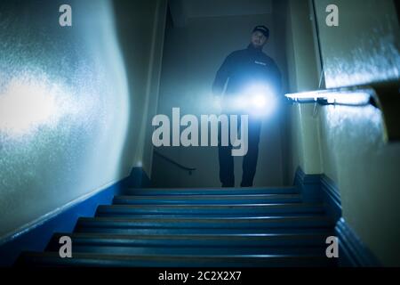 Male Security Guard Searching On Stairway With Flashlight Stock Photo