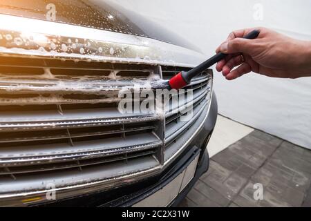 A close-up of the chrome shiny grille of the engine of a black expensive car covered with cleaning foam in service, the hand of a worker with a brush Stock Photo