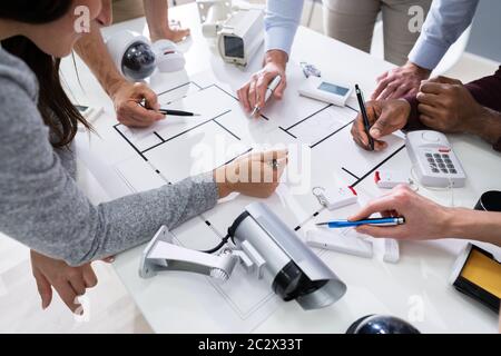 Group Of Security Engineers Working On Blueprint With Security Equipment On Table Stock Photo