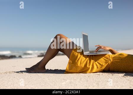 Mixed race woman using computer on the beach Stock Photo