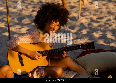 Young mixed race woman playing guitar and laughing on beach Stock Photo