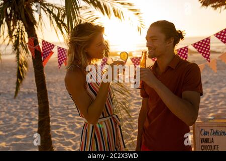 Caucasian couple smiling and drinking alcohol on beach Stock Photo