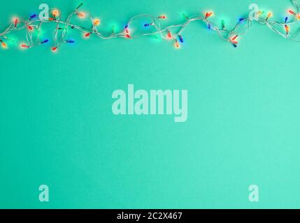 burning christmas garland on a white wire with colorful lights on a green background, copy space Stock Photo