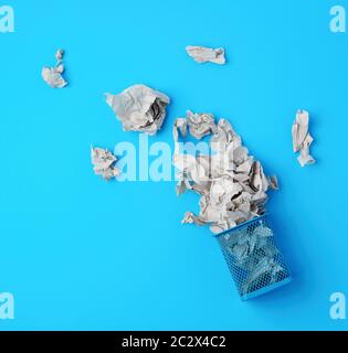overturned blue metal basket with crumpled pieces of paper, concept of recycling and pollution, blue background Stock Photo