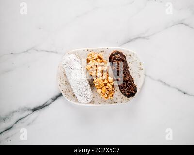Set of three homemade eclairs on marble background. Close up view of delicious healthy profitroles with different decor elements - chocolate, peanut a Stock Photo