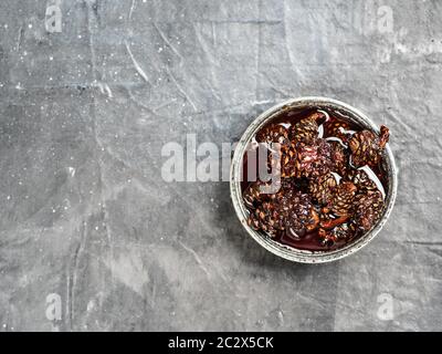 Delicious jam with baby pine cones in small bowl. Traditional Siberian dessert - young pine cones jam on gray textured background. Top view or flat la Stock Photo