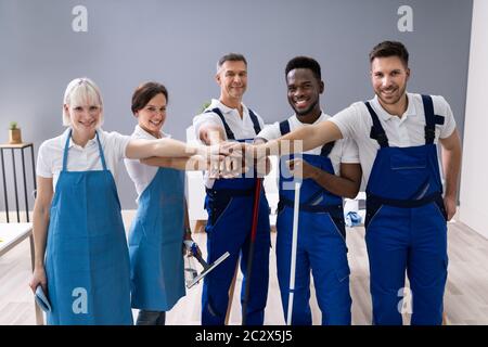 Portrait Of Happy Diverse Janitors In The Office With Cleaning Equipment Stacking Hands Stock Photo