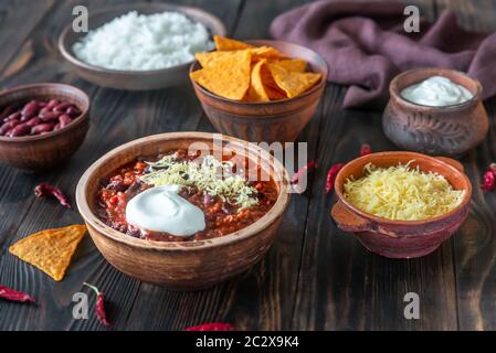 Bowl of chili con carne with toppings on a wooden table Stock Photo