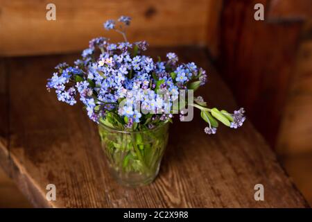 Blue wildflowers in a glass cup on a wooden background. Forget me nots. Stock Photo