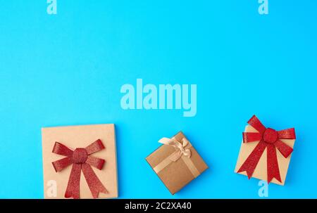 three closed square gift boxes with bows on a blue background, top view, place for text Stock Photo