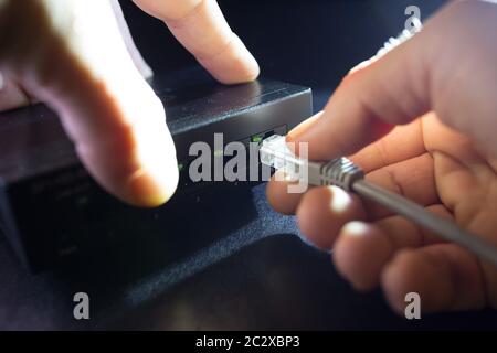 Close-up Hand holding ethernet cable on network switches background. Home network concept. Stock Photo