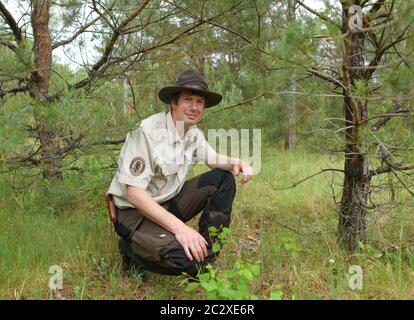 11 June 2020, Brandenburg, Müllrose: Nico Brunkow, ranger with the Brandenburg nature guard, squats in a forest in the Schlaubetal nature park. The smooth snake is an almost unknown creature in Germany. The second most common snake species after the grass snake lives mostly in hiding because of its grey-brown camouflage colouring. In the Schlaubetal, however, a ranger has been on its trail for years. At three checkpoints on the edge of the Schlaubetal near Müllrose (Oder-Spree), ranger Nico Brunkow carefully and with a searching eye lifts dozens of pieces of roofing felt or metal sheets that w Stock Photo