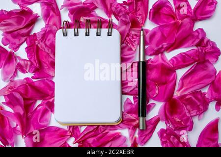 composition of blank notebook with pen on beautiful pink peony petals Stock Photo