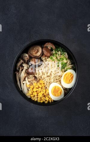 Ramen noodle soup. Soba noodles with eggs, shiitake and enoki mushrooms, corn and scallions, overhead shot on a black background Stock Photo