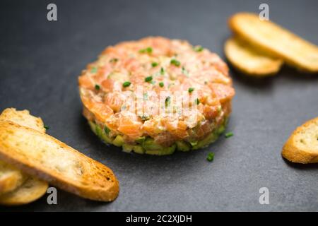 Salmon tartare is made with chopped fresh raw salmon fish, avocado, tartar sauce and crackers or bread. This healthy dish is often served as appetizer Stock Photo