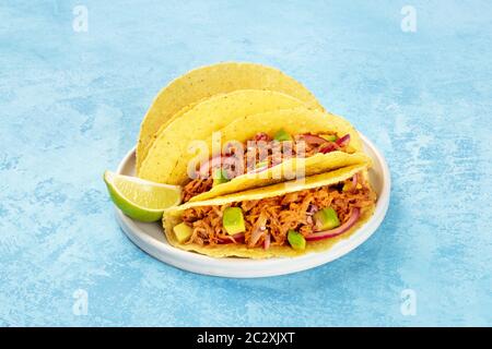 Cochinita pibil taco shells, a Mexican snack with pulled pork and avocado and marinated red onion, a close-up shot on a blue bac Stock Photo