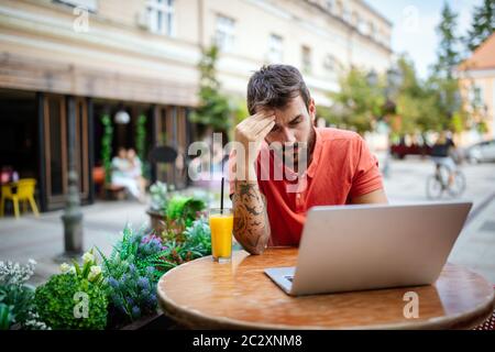 Pensive or worried young business man using laptop at cafe. Stock Photo