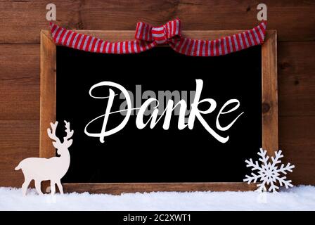 Chalkboard With German Calligraphy Danke Means Thank You. Christmas Decoration Like Deer And Bow. Wooden Background With Snow Stock Photo