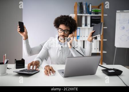 Smiling Young Businessman Doing Multitasking Work At Workplace Stock Photo