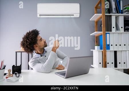 Young Businessman Operating Air Conditioner With Remote Controller In Office Stock Photo