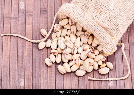 Close up shot of pistachios in a burlap sack spilled on wooden background. Stock Photo
