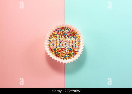 Cupcake liners with colored sugar inside from above. Flat lay top view. Confectionery cooking concept with copy space on bright blue and pink paper ba Stock Photo