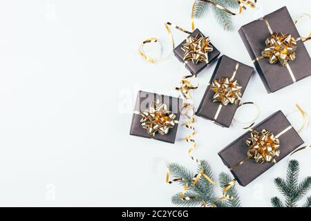 Christmas background black gift boxes with golden bows and ribbons next to green pine branches, flat lay. Stock Photo