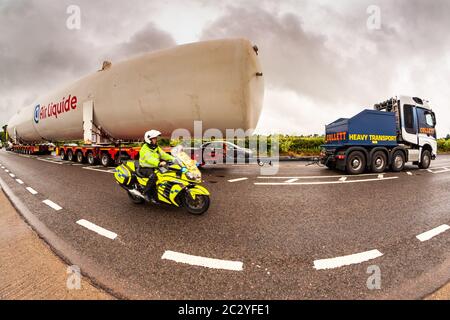 Shenstone, Staffordshire, UK. 18th June, 2020. A supersize oxygen tank - 40m long and 6.5m wide - is on its fourth day or transport across the midlands. Two cabs pulling and pushing, 156 wheels, four drivers, and many police and BT engineers and tree cutters are involved, as the enormous load goes from Cheshire to north Warwickshire. An 8mm fisheye lens just about managed to capture the scene. Credit: Peter Lopeman/Alamy Live News Stock Photo