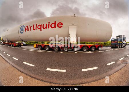 Shenstone, Staffordshire, UK. 18th June, 2020. A supersize oxygen tank - 40m long and 6.5m wide - is on its fourth day or transport across the midlands. Two cabs pulling and pushing, 156 wheels, four drivers, and many police and BT engineers and tree cutters are involved, as the enormous load goes from Cheshire to north Warwickshire. An 8mm fisheye lens just about managed to capture the scene. Credit: Peter Lopeman/Alamy Live News Stock Photo