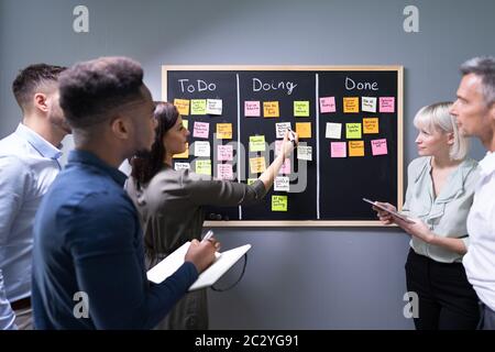 Group Of People Writing On Sticky Notes Attached To Blackboard In Office Stock Photo