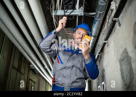 Male Worker Wearing Hard Hat Using Multimeter Stock Photo
