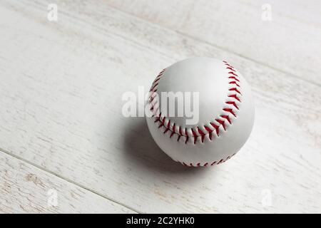 White baseball ball stitched with red thick thread made of genuine leather on a white wooden background. Stock Photo