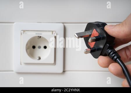 Hand Holding Incompatible AC Plug Near Wall Socket Stock Photo
