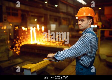 Master steelmaker in helmet at furnace with liquid metal, steel factory, metallurgical or metalworking industry, industrial manufacturing of iron prod Stock Photo
