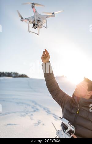Young man controlling his drone in snowy outdoors. Drone operator holding a transmitter and landing with a drone. Stock Photo