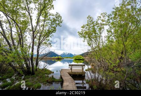Jetty with wooden bench at the lake, mountains reflected in the lake, Glenorchy Lagoon, Glenorchy, near Queenstown, South Island, New Zealand Stock Photo