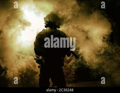 Silhouette of modern infantry soldier, elite army fighter in tactical ammunition and helmet, standing with assault service rifle in hands on backgroun Stock Photo